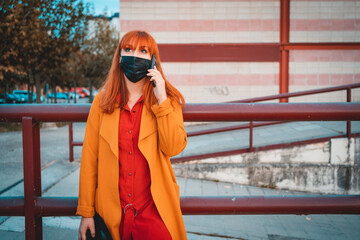 beautiful elegant girl in a black medical mask on her face, dressed in a orange coat, talking on a mobile phone, Coronavirus, quarantine