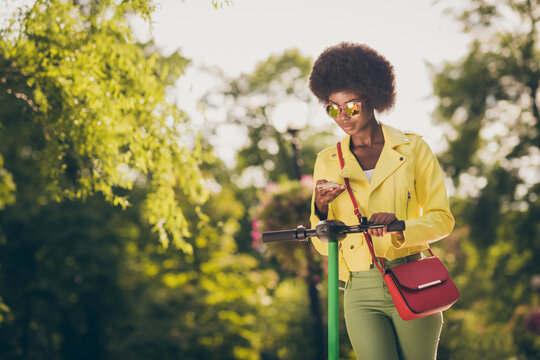 Photo Portrait Of Hipster Girl Driving Kick-scooter Checking Phone Holding In One Hand In Park