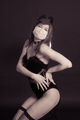A young woman in a black bodysuit and medical mask, moves and dances. Studio photo on a black background