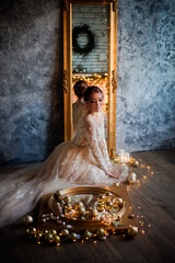 beautiful young girl in gold glamorous near christmas balls and toys looks in the mirror