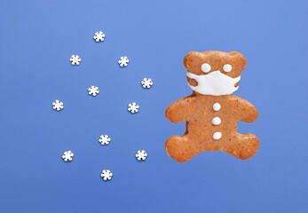 Gingerbread bear with protective face mask isolated on blue background with small sugar snowflakes. Christmas or New year concept. Coronavirus winter