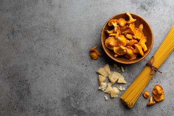 Wild forest mushrooms chanterelles in wooden bowl, raw pasta spaghetti and parmesan. Seasonal autumn food, ingredients for cooking fresh chanterelles pasta. Copy space, food background top view