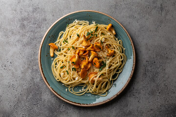 Pasta spaghetti with wild forest mushrooms chanterelles on plate. Seasonal autumn dish on rustic concrete background from above. Meal with aromatic fall chanterelles