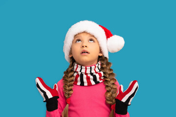 A little girl in a Christmas hat looks up in surprise on a blue background.
