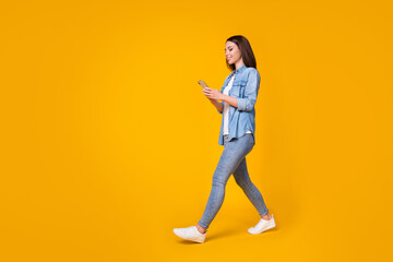 Fototapeta na wymiar Full body profile photo of attractive cheerful lady good mood walk down street chatting telephone friends meeting wear casual denim shirt sneakers isolated vivid yellow color background