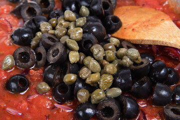 Cooking spaghetti alla vesuviana, pasta with sauce and tomatoes, olives, onions and capers - Cooking sauce from onions, chopped tomatoes, olives and capers in a frying pan close-up