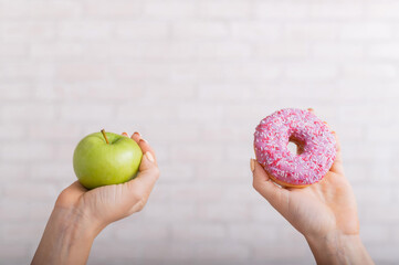 Donut and green apple in female hands. The concept of different eating habits. Thinness and obesity
