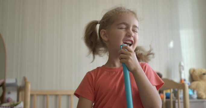 Little Fun Creative Girl Singing and Using Broom Handle as Microphone. Child Using Mop as Microphone While Singing in Domestic Room. Enjoying Spring Cleaning. Playful Creative Kid Dancing With Mop.