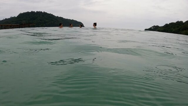 group of asian tourist playing in the sea. light rain droplet drop into calm sea water at tropical island. female friends talking in the sea. 