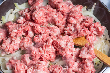 Cooking tortiglioni with onion and sausage stew, pasta with sausage sauce with onions and tomato paste - cooking onion and sausage stew in a pan, close-up