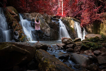 Serenity with young man yoga practicing in the Autumn Forest and Waterfall background