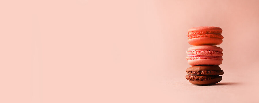 Pink and brown french dessert macaroons on a pastel pink background with copyspace