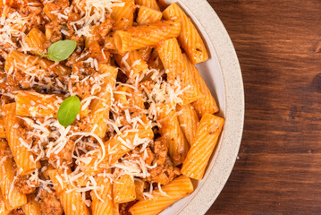 Cooking tortiglioni with onion and sausage ragout, pasta with sausage sauce with onions and tomato paste, sprinkled with tertum cheese on a plate on a rustic wooden table, top view, copy space