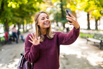 Happy woman waving hand greeting during a phone video call in the street