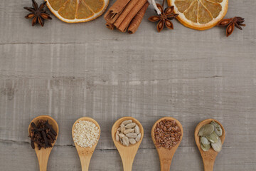 Seeds on wooden spoons. Top view of dried orange, cinnamon, star anise on gray background