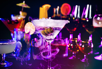 Martini drink with olives at bar counter close up. Bartender show and prepared cocktail with dry ice on a cocktail bar background. Colorful various drinks in a bar with dry ice smoke effect.