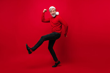 Fototapeta na wymiar Full-length portrait of bearded old man dancing in new year. Santa claus having fun on red background.