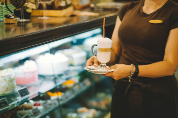 Barman barista in uniform serves coffee cocktails at the restaurant. Irish coffee in glass holds a barista in his hands. Coffee cocktail with milk in a glass