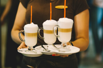 Barman barista in uniform serves coffee cocktails at the restaurant. Irish coffee in glass holds a barista in his hands. Coffee cocktail with milk in a glass
