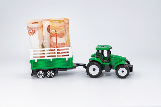 A toy green farm tractor carries five-thousand-ruble bills rolled into a tube in a trailer