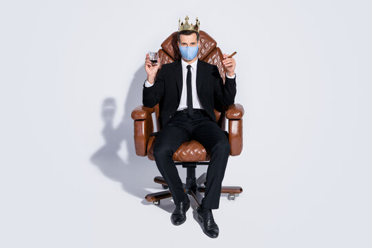 Full body photo of handsome business guy sit office chair hold whiskey glass cuban cigar golden crown wear blue fabric face mask isolated grey background