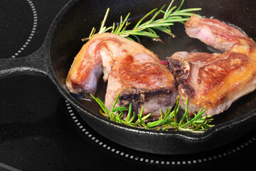 Lamb loin chops with rosemary in a cast iron frying pan.  Cooking on an electric hob stove
