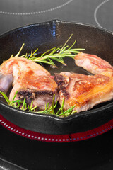 Lamb loin chops with rosemary in a cast iron frying pan.  Cooking on an electric hob stove
