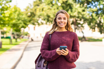 Attractive young woman uses her phone walking down the street in the city