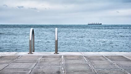 Obraz premium Concrete pier with steel ladder in the sea with ship