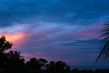Fototapeta na wymiar Dramatic colorful clouds over trees and sea on a tropical island