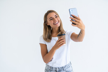 Young beautiful woman using smartphone selfie time, holding coffee cup and mobile phone isolated on white background.. Lifestyle concept.