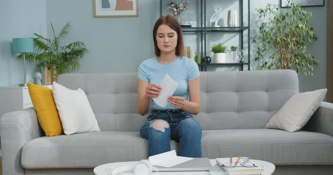 Good-looking Young Female Receiving Letter From Friend, Family Indoors. Pretty Caucasian Woman Opening, Reading Message And Being Happy In Living Room At Home. Mail, Postcard Concept.