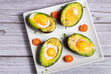 Aguacate con huevos al horno con tomates de cherry sobre un plato blanco
