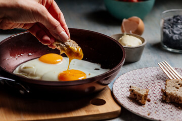 hand dips bread in the fried egg, in the pan