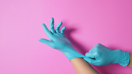 Hand is pulling surgical gloves or blue latex gloves on pink background.