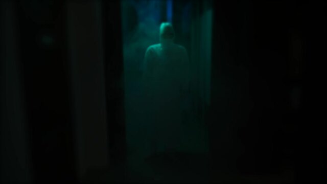 Dark blurred hospital corridor with a silhouette of a man in coverall. Stock footage. Unrecognizable person in protective suit, interior of a horror quest room.