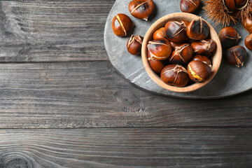 Delicious roasted edible chestnuts on black wooden table, top view. Space for text