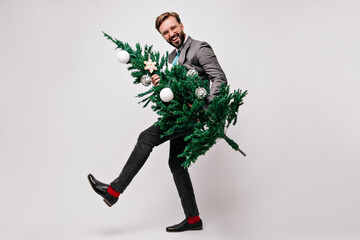 Full-length portrait of brunette man enjoying new year party. Stylish guy holding green christmas tree.