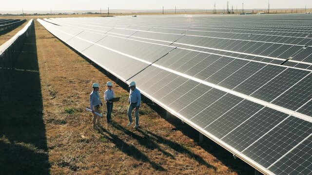 Engineers walking between rows of solar panels. Solar power plant workers, solar energy industry concept.