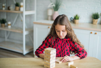 Portrait of teen curly girl playing in wooden game alone in kitchen