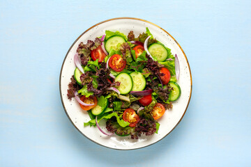 Healthy vegetable salad of cherry tomatoes, cucumber slices, green and purple lettuce leaves, onions and olive oil in plate on blue wooden table Top view Flat lay Diet, mediterranean menu Vegan food