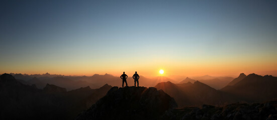 Two Men reaching summit enjoying freedom and looking towards mountains sunset. - 388988235