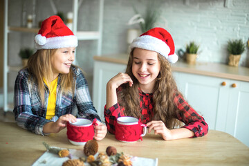 Two happy caucasian girls in red santa claus hats in the kitchen playing and smiling