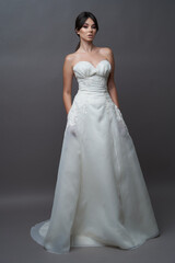 Fototapeta na wymiar Beautiful bride in wedding dress posing on grey background with copy space.