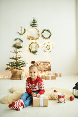 Fototapeta na wymiar portrait of a beautiful little girl in a red Christmas sweater with reindeer on a white peel with a lantern and gifts