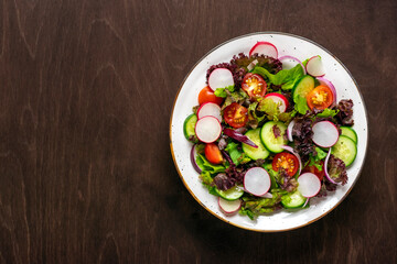 Healthy vegetable salad of cherry tomatoes, cucumber slices, green and purple lettuce leaves, onions and olive oil in plate on wooden table Top view Flat lay Diet, mediterranean menu Vegan food