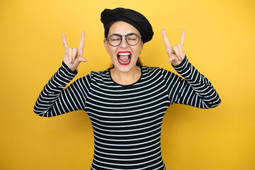 Young beautiful brunette woman wearing french beret and glasses over yellow background shouting...