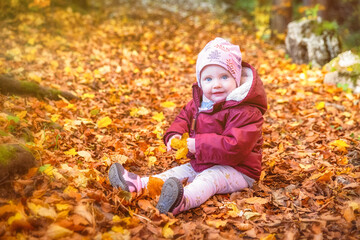 Happy liitle baby sitting on colorful leaves in forest