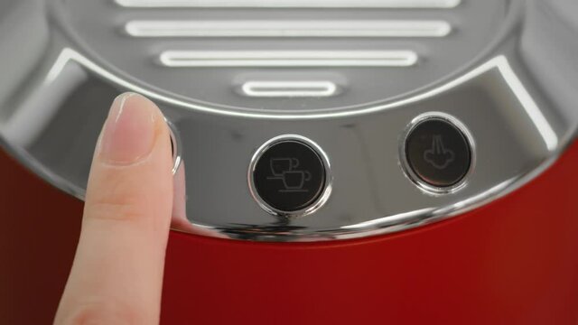 Close up of a finger pressing espresso coffee button on a bright red and chrome coffee machine at home with signs of coffee blinking