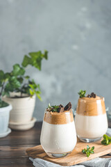 Two glasses with Dalgona frothy coffee trend korean drink latte espresso with coffee foam, decorated by thyme and dark chocolate. Dark wooden table surface